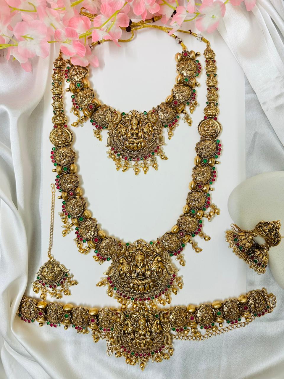 Ornate gold necklace with red and green stones on a white fabric background