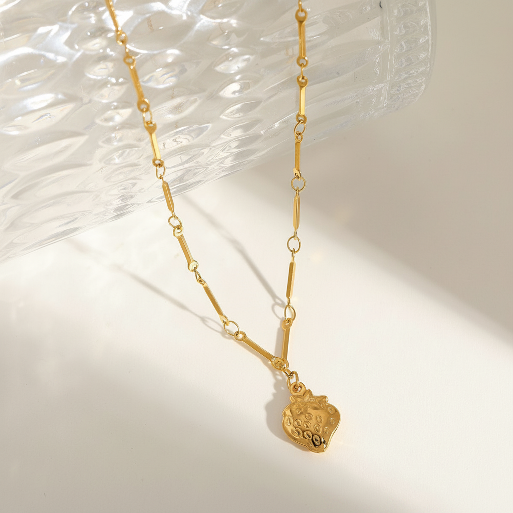 Gold strawberry pendant necklace with bar-link chain on white surface